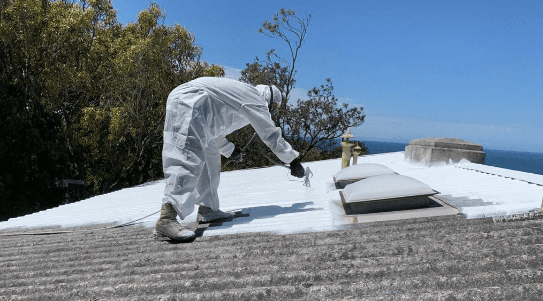 Worker in protective coveralls sealing a corrugated asbestos roof